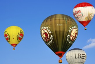 Four hot air balloons with lots of colourful advertising rise into the air with passengers on