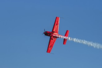 Red stunt aerobatic plane performing stunts in blue sky. Concept of speed, difficulty, precision,