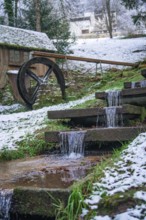 A small water wheel with a snow-covered stream in picturesque winter, spa garden, Bad Wildbad,