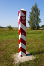 Polish red and white border post on a green meadow under a sunny sky, border with Ukraine,