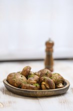 A wooden plate filled with roasted mushrooms garnished with herbs on a rustic table. A pepper mill