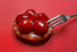 Strawberry tartlet with fork on red background, fruit cake