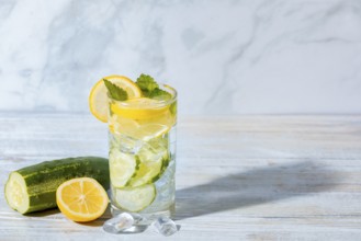 A glass of cucumber water with lemon slices, mint leaves and ice cube cubes, cucumber and lemon on