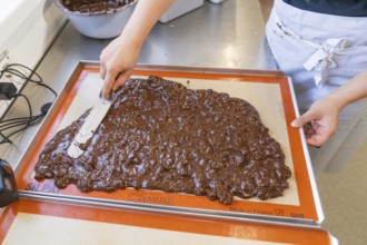 A person spreads and smoothes chocolate with a spatula on a baking mat, Burch Schokolade