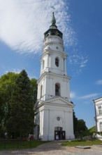 White baroque church tower with greenery in a picturesque setting under a blue sky, bell tower of