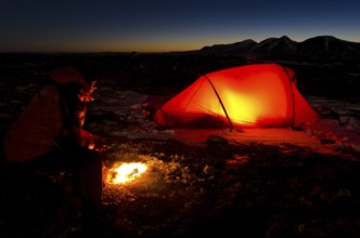 Man with campfire and lit tent, Engerdalsfjellet, Rendalssölen peak in the background, Hedmark