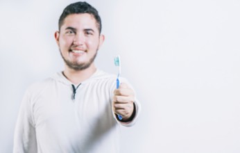 Young man holding toothbrush and looking at camera isolated. Oral health concept