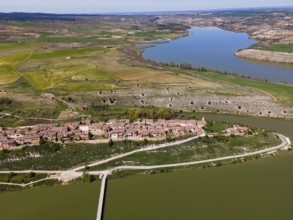 Aerial view of a river meandering through a green landscape with a village and a bridge in the