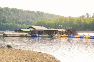 A lake with a jetty for boats and surrounded by huts and forest, Rappbodetalsperre, Harz, Germany,