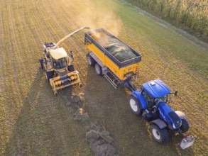 Aerial view of a tractor and a harvester collecting hay in a field. Yellow and blue machines,