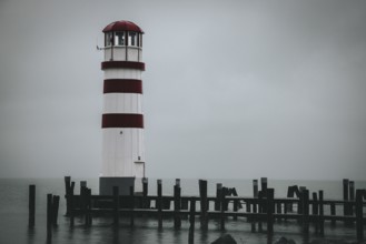 A red and white lighthouse stands on the lake on a foggy day, Podersdorf, Burgenland, Austria,