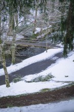 Snowy landscape with a wooden bridge over a river, embedded in a wintry forest, spa gardens, Bad