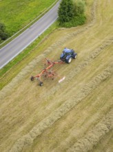 Aerial view of a blue tractor with hay machine in a field, near a road, Dachtel. Black Forest,