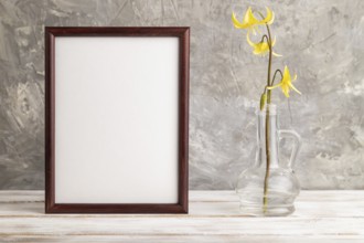 Wooden frame with yellow trout lily or dogtooth violet flowers in glass on gray concrete background