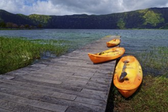 Three orange kayaks on the wooden jetty of the crater lake Lagoa Azul, surrounded by greenery and