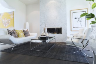 Living room with white leather and chrome sofa, armchairs, glass-top coffee table, gas fireplace