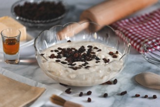 Bowl with curd cheese cream and sultanas, surrounded by ingredients and kitchen utensils