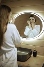 Reflection in the mirror of a woman with mineral sheet mask on her face in bathroom