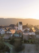 A small village with half-timbered houses and a church in the morning light, surrounded by forests,