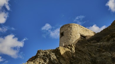 Ruin of a windmill, Stone tower on a rock, surrounded by blue sky and clouds, Colourful mountain