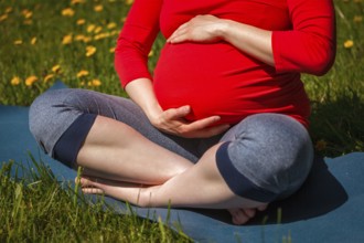 Pregnancy yoga exercise, pregnant woman doing asana Sukhasana easy yoga pose holding her abdomen