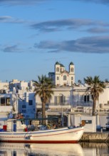 Fishing boats in the harbour at sunset, reflected in the sea, White Cycladic houses and church