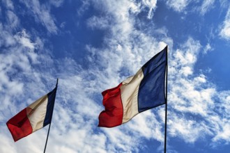 Two French national flags fluttering side by side in the wind, tricolour, slightly cloudy sky,