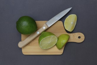 Halved limes on a chopping board with a kitchen knife