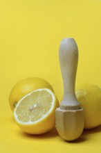 Halved lemon with citrus juicer against a yellow background