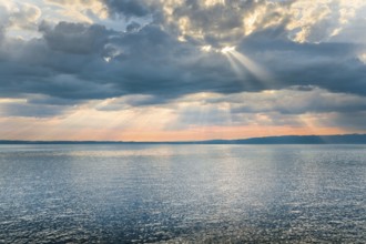 Tyndall effect over Lake Constance, sun rays break through cloudy sky and reflect on the water,