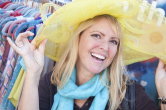 Happy blonde woman playfully modeling a big sun hat at the market