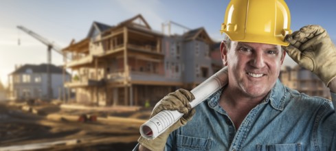 Friendly male contractor at a construction site wearing a hard hat and work gloves holding his