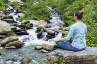 Woman doing yoga meditation asana Padmasana lotus pose outdoors at tropical waterfall