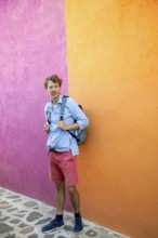 Young man in front of pink and orange house wall with backpack, colourful houses on the island of