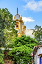 Baroque church tower rising through vegetation and buildings in the city of Tiradentes in the state