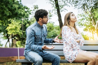 Upset couple arguing in a park. A young couple arguing sitting on a park bench, Concept of couple