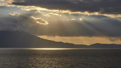 Dramatic cloudy evening sky, sun rays breaking through clouds, sun reflection on the sea, sunset,