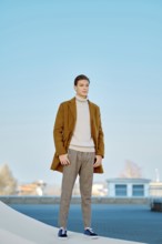 Spring, autumn outfit. Street fashion. Young man in checkered trousers, sweater and wool coat