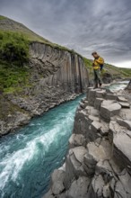 Tourist standing by the river in Stuðlagil Canyon, turquoise blue river between basalt columns,