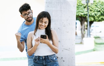 Jealous man spying on his girlfriend texting on the cell phone. Suspicious man spying on his