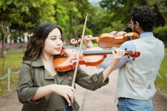 Two young violinists standing playing violin in a park. Portrait of man and woman together playing