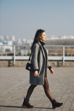 Young woman walking along the street in sunny day in spring-autumn casual outfit