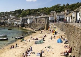 People on crowded beach in Mousehole village, Cornwall, England, UK