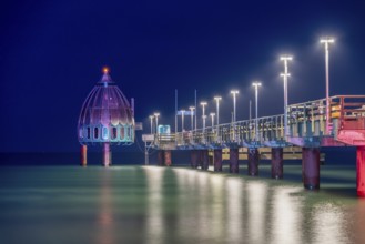 Diving gondola and long illuminated pier in the sea at night, calm water reflects lights, Zingst,