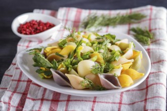 Conchiglie colored pasta with fresh greengrocery on a linen tablecloth on black wooden background.