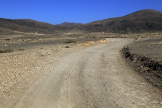 Dirt road crossing dry barren mountain landscape near Paraja, Fuerteventura, Canary Islands, Spain,