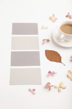 Composition with gray paper business card, brown beech autumn leaves, hydrangea flowers and cup of