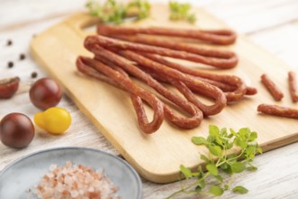 Traditional polish smoked pork sausage kabanos on cutting board with salt and pepper on white