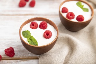 Yogurt with raspberry in clay cups on white wooden background and linen textile. Side view, close