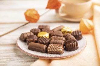 Chocolate candies with cup of coffee and physalis flowers on a white wooden background and orange